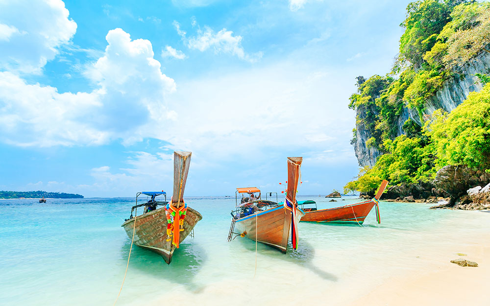 a beach in phuket in asia with boats on the sea, a place you can visit on a asia cruise